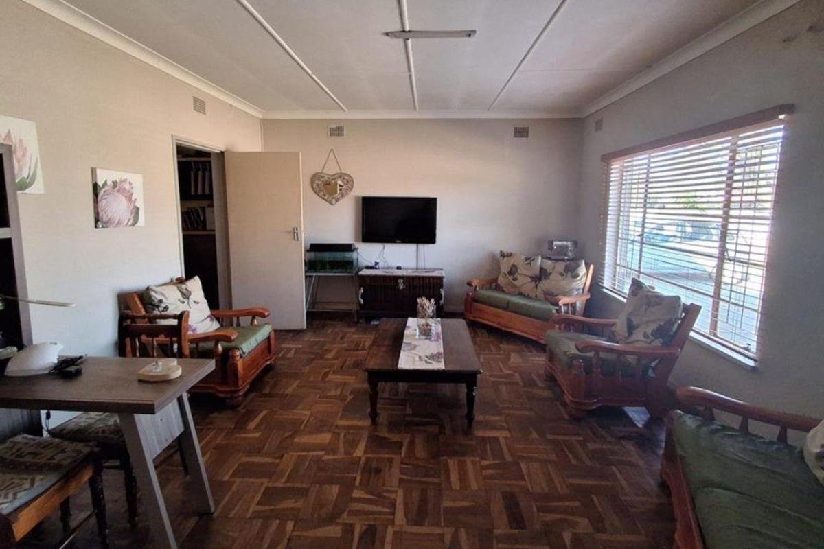 A spacious living room featuring traditional parquet flooring, large windows with venetian blinds, and classic ceiling tiles.