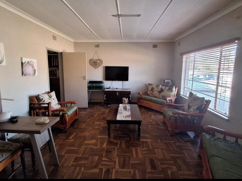 A spacious living room featuring traditional parquet flooring, large windows with venetian blinds, and classic ceiling tiles.