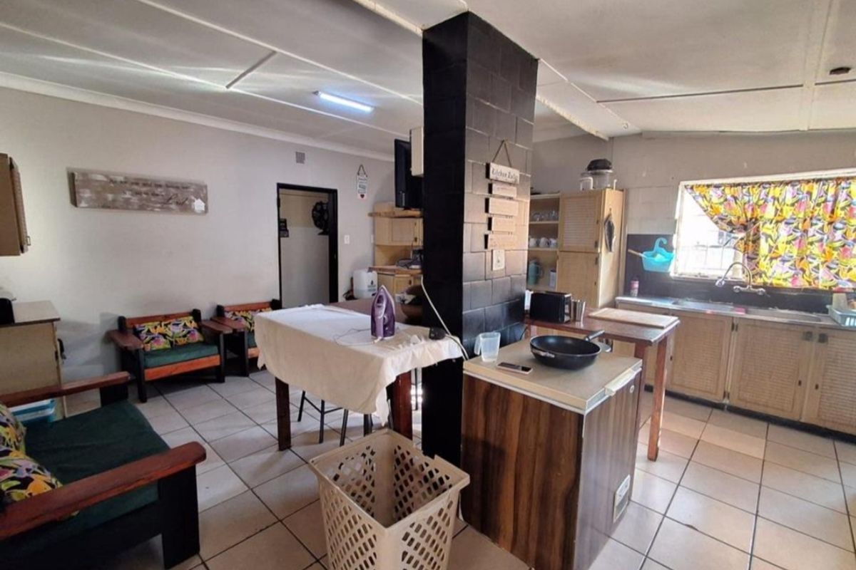 Open-plan living and kitchen area featuring tiled flooring, a central brick pillar, and functional kitchen cabinetry in need of modernization.