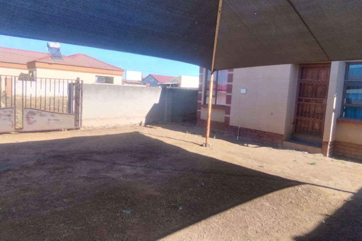 Rear exterior area featuring a shade sail, perimeter wall, and metal gate access, with an unpaved yard space.