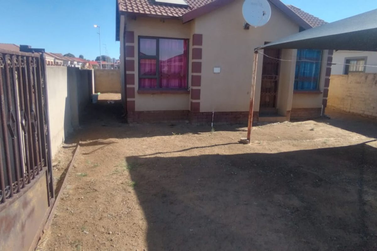 Front exterior view of the house featuring a wrought iron gate, perimeter wall, and a shade cloth carport structure over the yard area.
