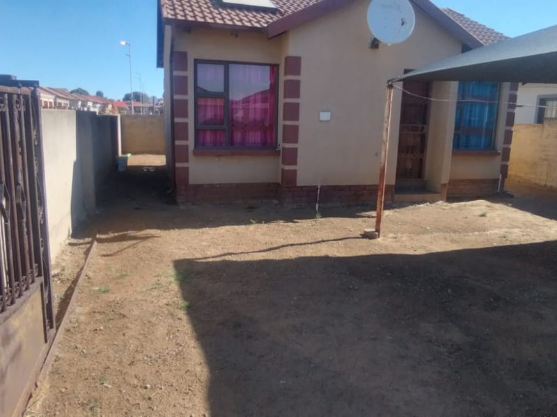 Front exterior view of the house featuring a wrought iron gate, perimeter wall, and a shade cloth carport structure over the yard area.