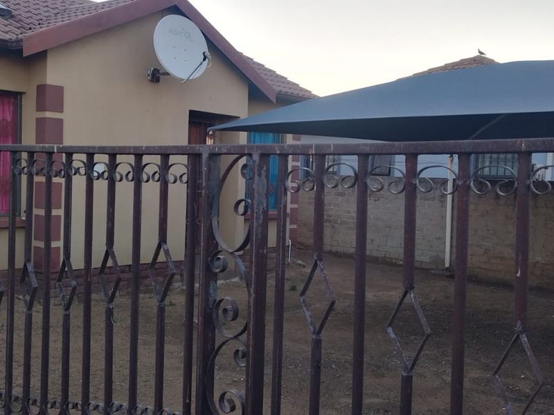 Front view of a residential property featuring a wrought iron gate, tiled roof, and a shade cloth carport structure.