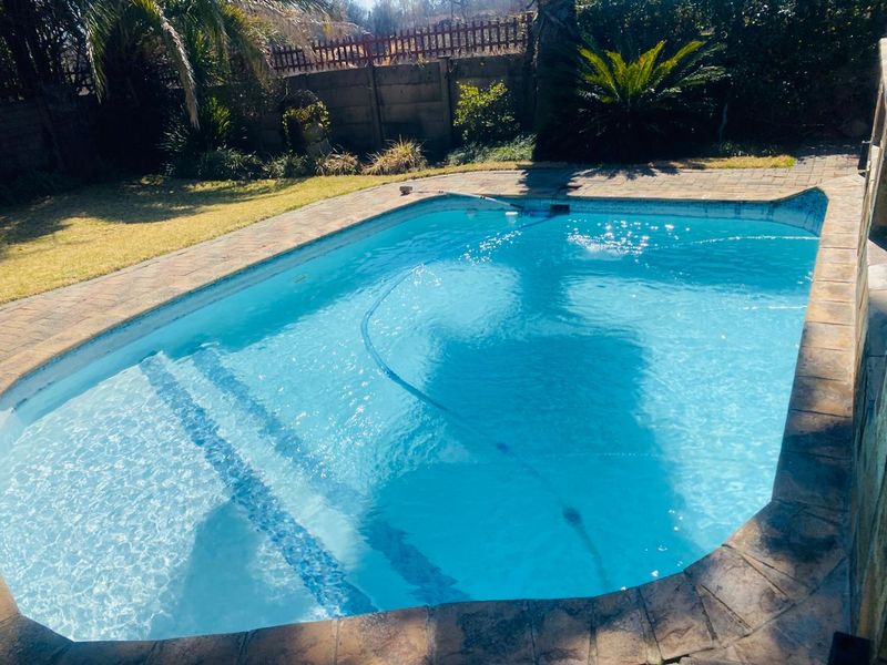 A private swimming pool area featuring a paved surround, established garden, and boundary wall, providing a functional outdoor space for recreation.