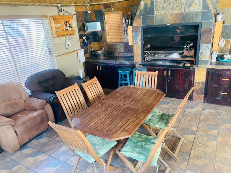 Covered outdoor patio area featuring a built-in braai, stone tile finishes, and built-in cabinetry with a sink, ideal for entertaining.