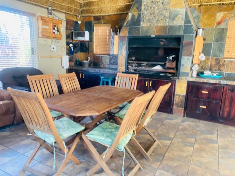 Covered patio area featuring a built-in braai, stone wall cladding, thatched ceiling, and built-in cabinetry with a sink.