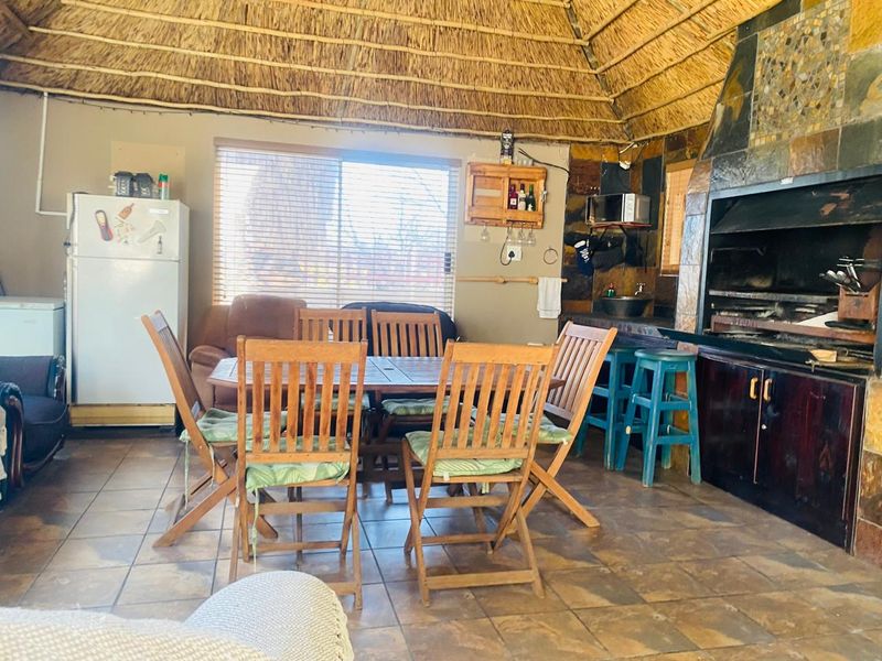 Covered outdoor entertainment area featuring a traditional thatched roof, built-in braai with stone cladding, and tiled flooring, ideal for social gatherings.