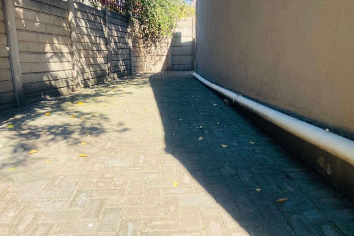 A narrow paved side passage or rear exterior area featuring boundary walls and an external drainage pipe.