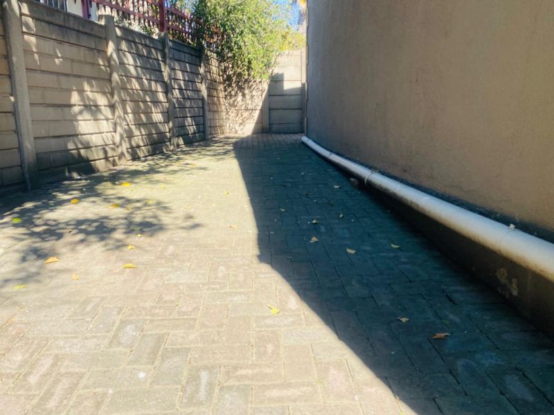 A narrow paved side passage or rear exterior area featuring boundary walls and an external drainage pipe.