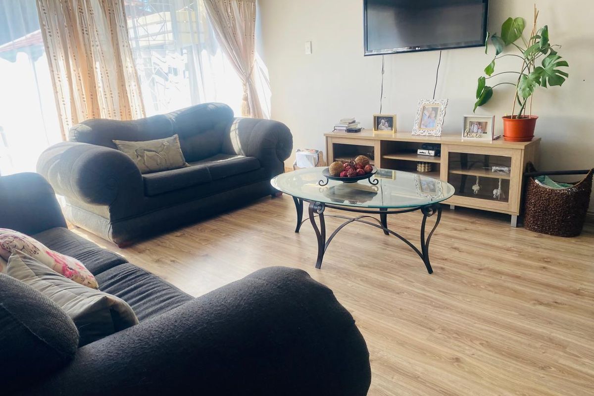 A comfortable living room featuring light-toned laminate flooring and large windows with curtain rails, providing a bright and functional space.