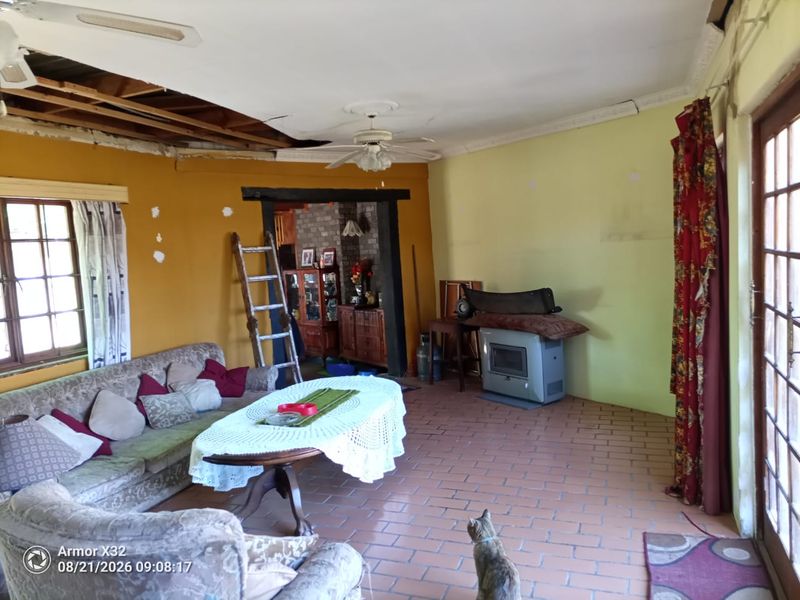 Living room featuring brick flooring, a freestanding fireplace, and exposed ceiling sections requiring repair and renovation.