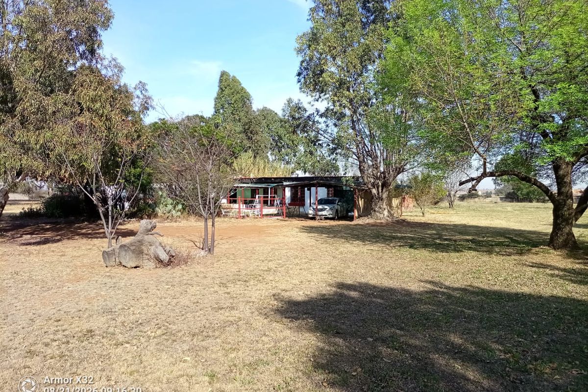 A view of the rear exterior of the farm property featuring a covered patio area surrounded by mature trees and open land.
