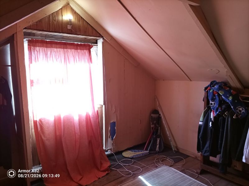Attic-style bedroom featuring a pitched ceiling and timber wall paneling, currently requiring cosmetic repairs to the wall surfaces.