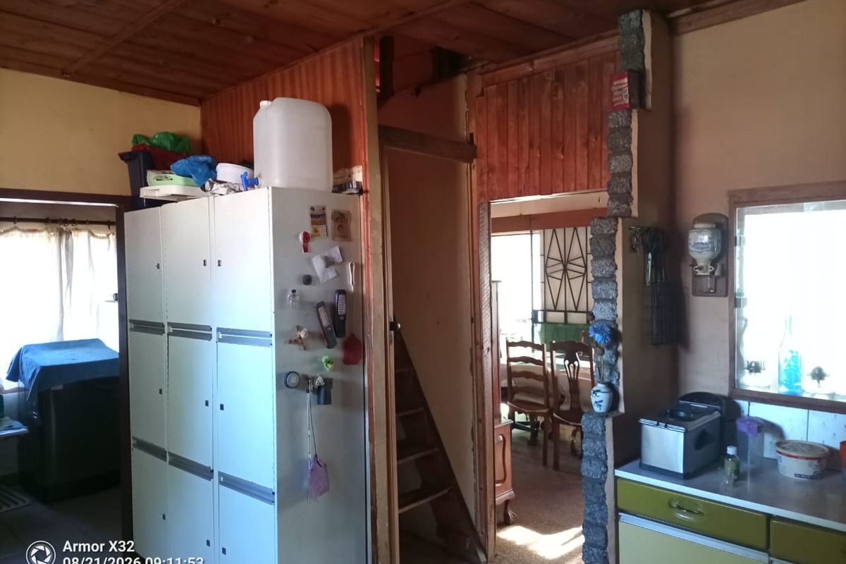 A rustic kitchen area featuring wooden ceilings, a stone-clad pillar, and built-in cabinetry, showing signs of age and requiring modernization.