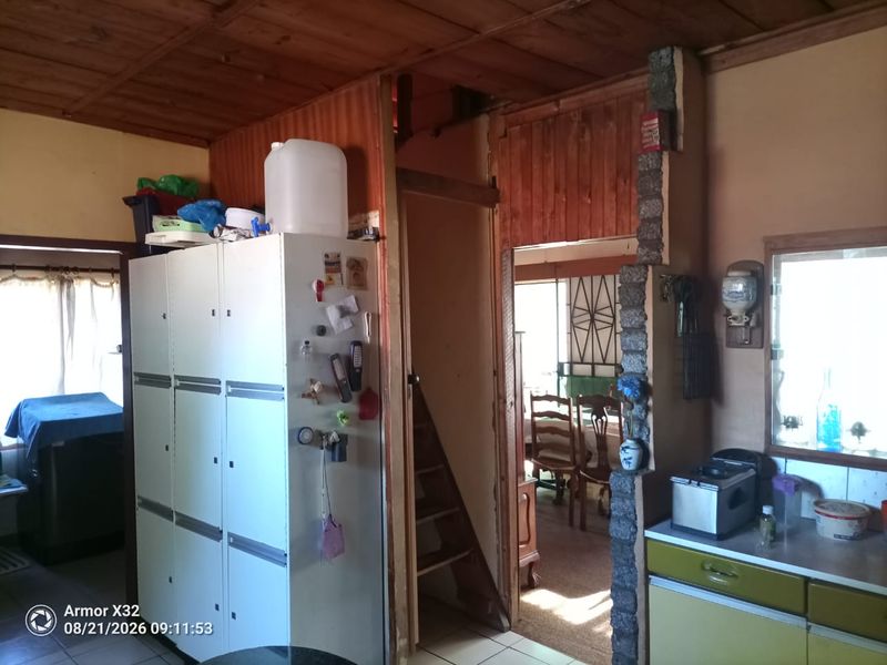 A rustic kitchen area featuring wooden ceilings, a stone-clad pillar, and built-in cabinetry, showing signs of age and requiring modernization.