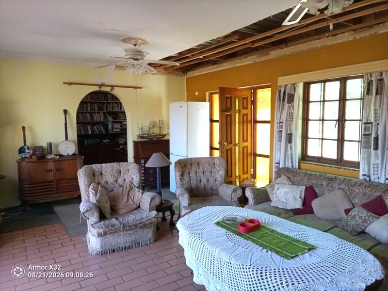 Living room featuring terracotta tile flooring, an arched doorway, and timber framed windows, currently requiring significant ceiling and wall repairs.