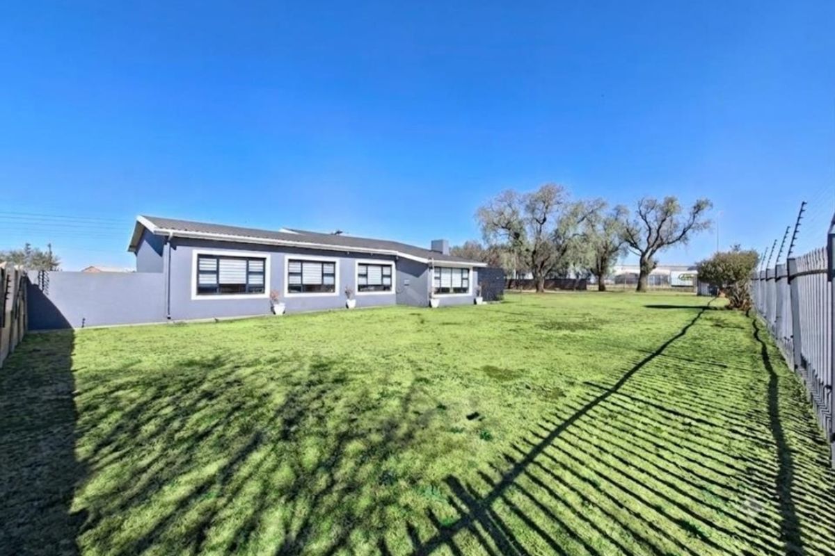 Spacious rear garden featuring a large lawn area, perimeter wall with electric fencing, and a view of the rear elevation of the house.