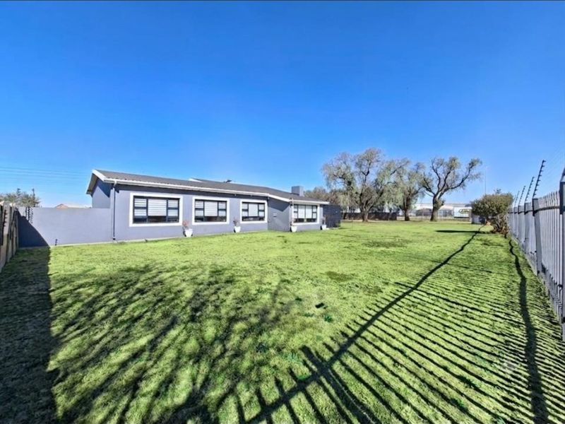 Spacious rear garden featuring a large lawn area, perimeter wall with electric fencing, and a view of the rear elevation of the house.