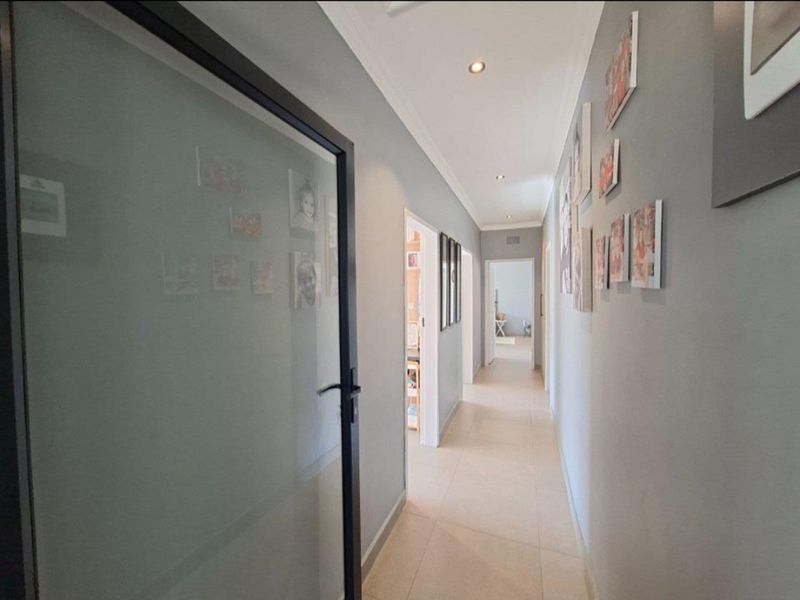 A bright and well-maintained hallway featuring neutral tiled flooring, recessed downlighting, and a modern frosted glass door leading to adjacent rooms.