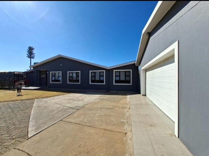 Front elevation of a modern house featuring a double garage, concrete driveway, and security shutters on the windows.