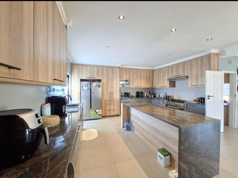 Spacious modern kitchen featuring extensive wood-finish cabinetry, a large central island with stone countertops, and integrated gas cooking appliances.