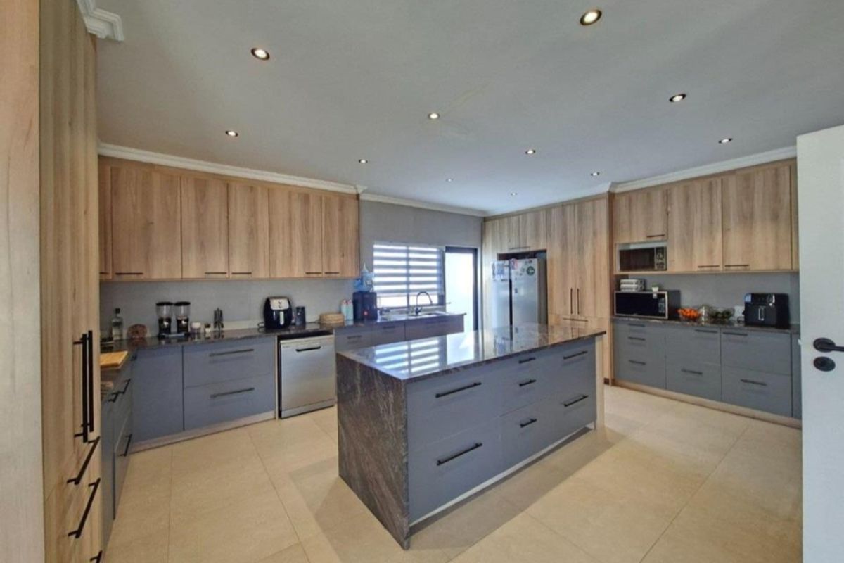 Modern kitchen featuring a large central island with stone countertops, extensive built-in cabinetry, integrated appliances, and recessed lighting throughout.