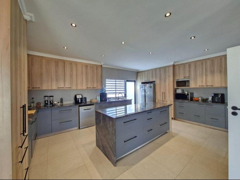 Modern kitchen featuring a large central island with stone countertops, extensive built-in cabinetry, integrated appliances, and recessed lighting throughout.