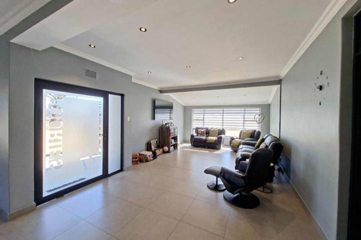 Spacious living room featuring neutral tiled flooring, recessed downlighting, and a modern frosted glass entrance door.