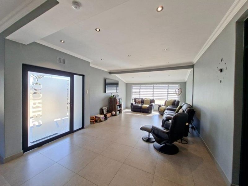 Spacious living room featuring neutral tiled flooring, recessed downlighting, and a modern frosted glass entrance door.