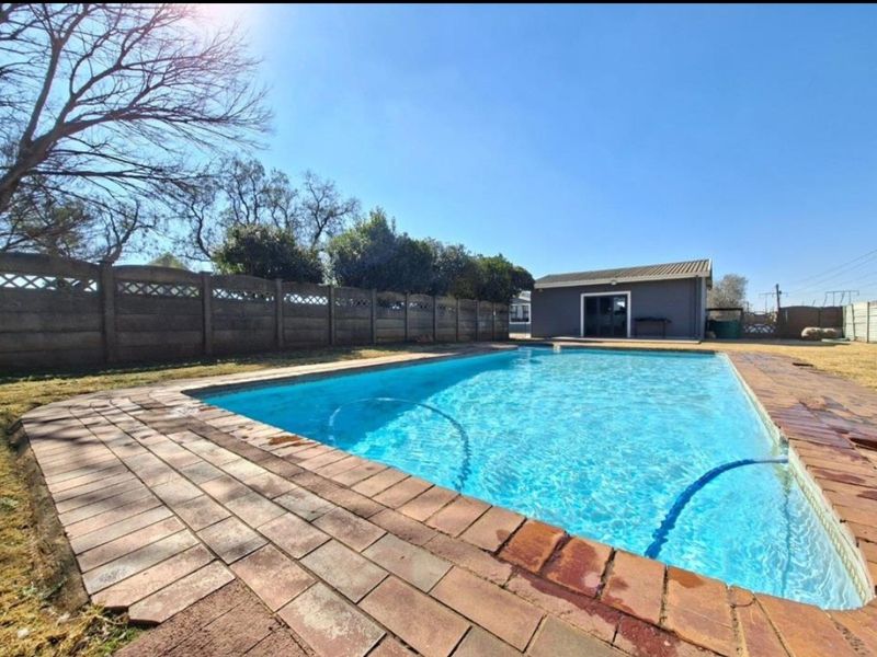 Outdoor pool area featuring a swimming pool with brick paving surround, enclosed by a precast concrete boundary wall and a detached outbuilding.