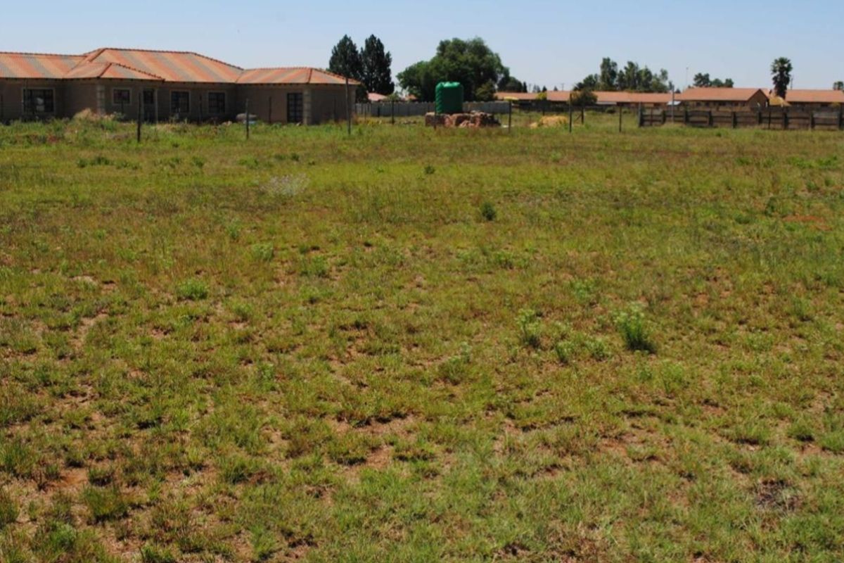A view of a vacant residential plot featuring natural grass coverage, perimeter wire fencing, and a water storage tank.