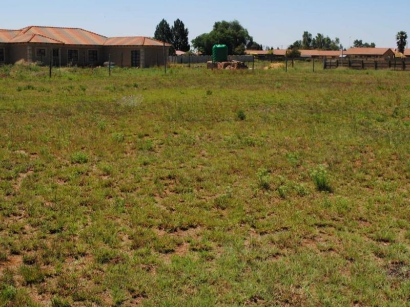 A view of a vacant residential plot featuring natural grass coverage, perimeter wire fencing, and a water storage tank.