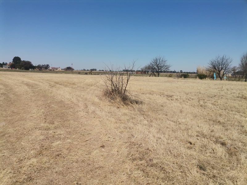 A wide-angle view of a vacant residential plot featuring dry grassland and open space, suitable for future development.