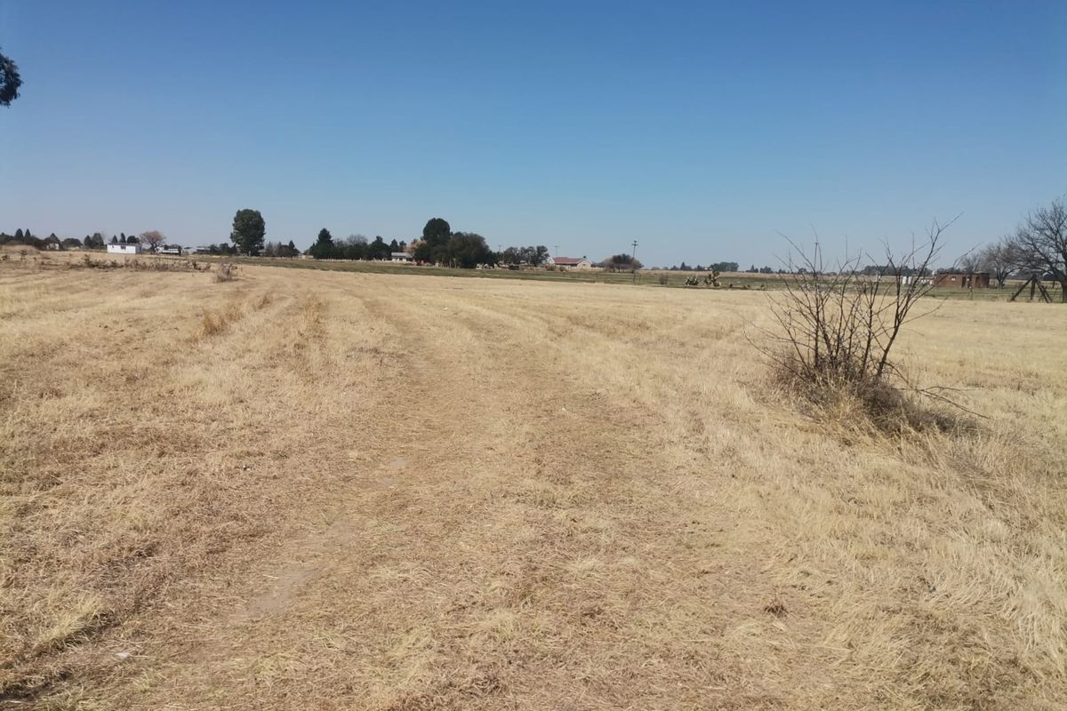 A view of a large, open, vacant residential plot featuring dry grassland and a clear horizon.