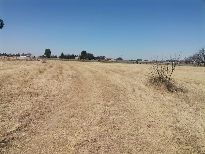A view of a large, open, vacant residential plot featuring dry grassland and a clear horizon.