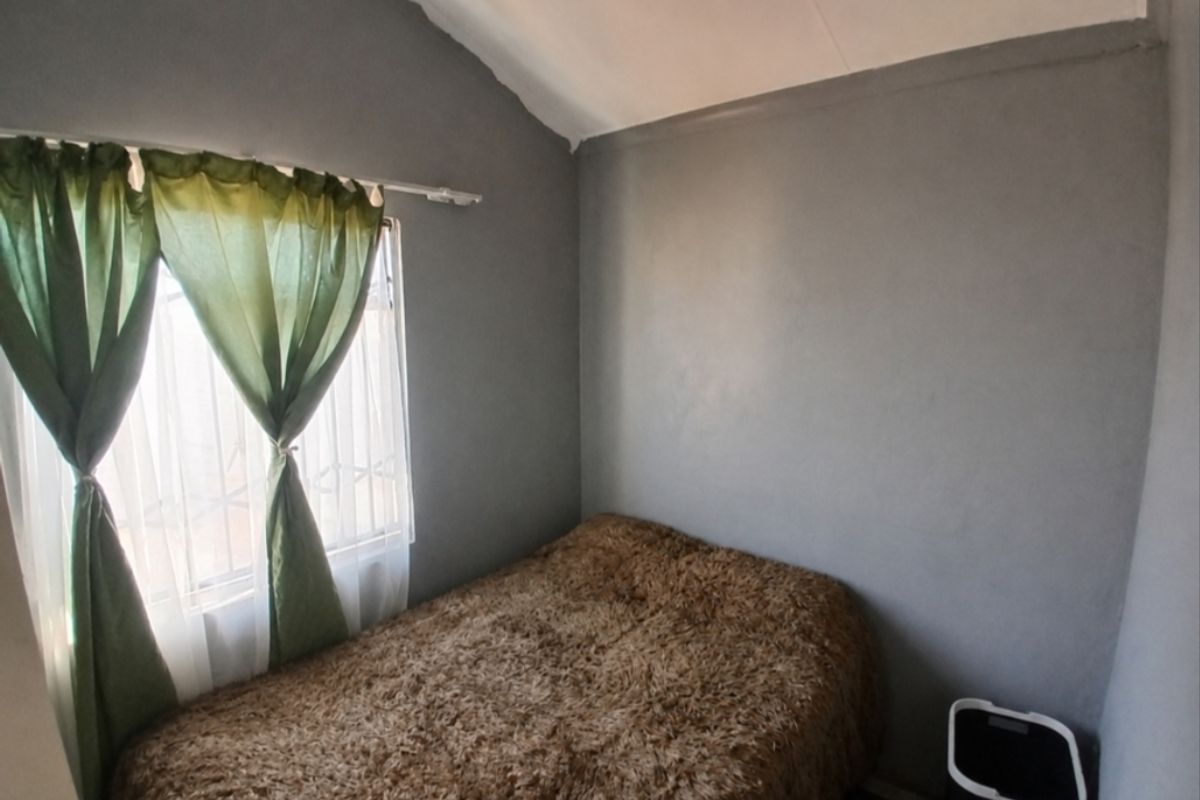 A compact bedroom featuring grey painted walls, a vaulted ceiling, and a window with fitted curtain hardware.
