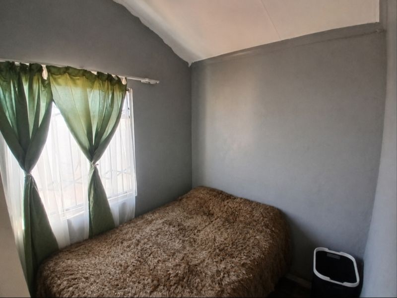 A compact bedroom featuring grey painted walls, a vaulted ceiling, and a window with fitted curtain hardware.
