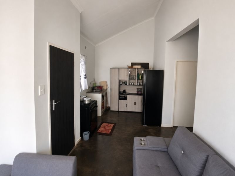 An open-plan living and kitchen area featuring vaulted ceilings, tiled flooring, and built-in cabinetry with a functional sink and prep space.