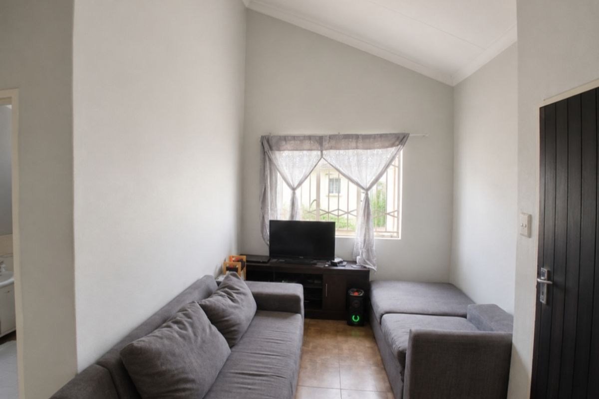 A living room featuring a high vaulted ceiling, tiled flooring, and a window fitted with security bars.