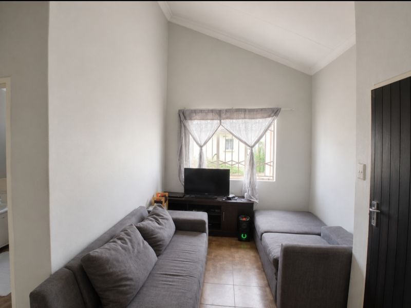 A living room featuring a high vaulted ceiling, tiled flooring, and a window fitted with security bars.