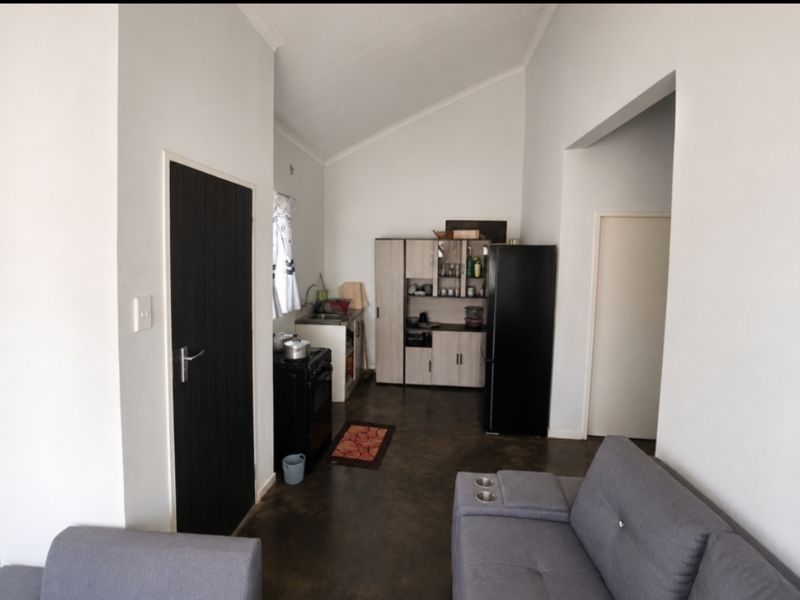 Open-plan living area featuring a compact kitchen with built-in cabinetry, a freestanding stove, and vaulted ceilings with polished concrete flooring.