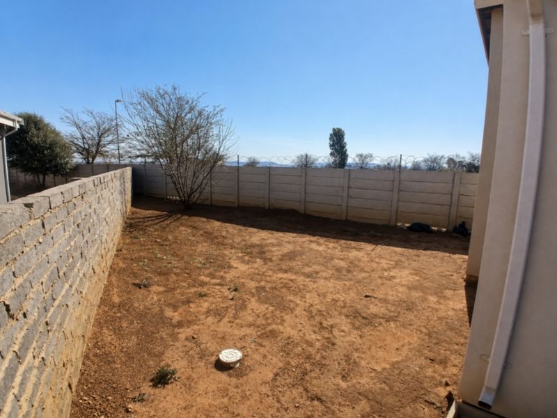 A private rear garden area featuring a precast concrete boundary wall with security razor wire and an open, unlandscaped yard space.