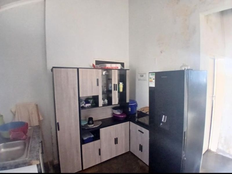 A small kitchen area featuring built-in cabinetry and a stainless steel sink, showing signs of wall water damage and wear.