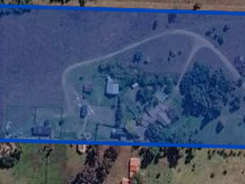 Aerial view of a large residential vacant land plot featuring existing outbuildings, internal driveway access, and established boundary fencing.