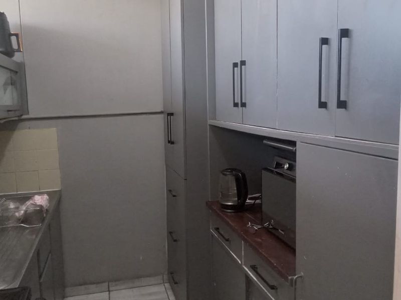 A functional scullery area featuring built-in grey cabinetry, a stainless steel sink, and tiled splashback, providing additional storage and prep space.