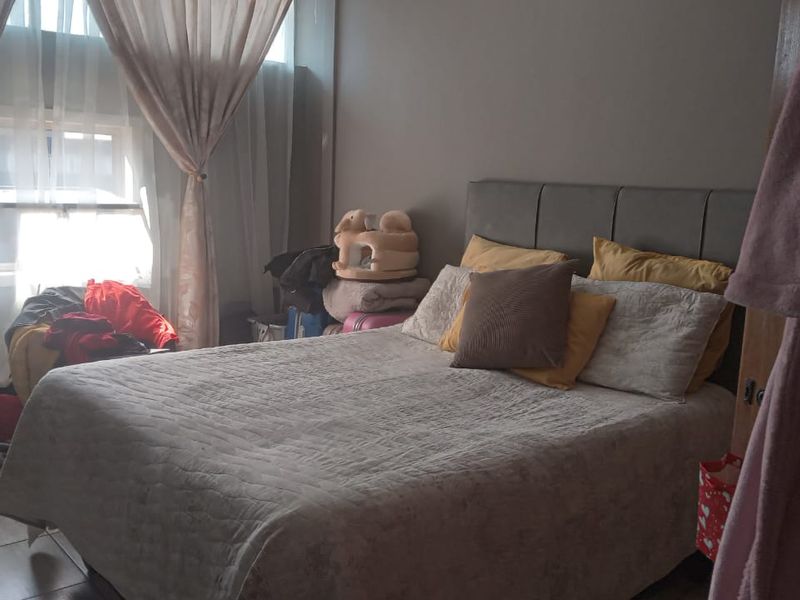 A bedroom featuring tiled flooring and a large window with curtains, providing natural light to the space.