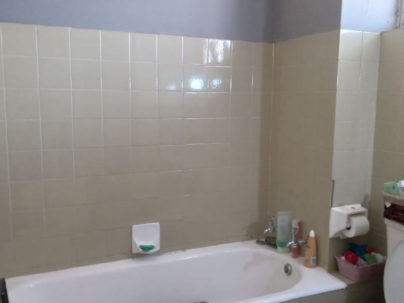 A functional bathroom featuring a standard bathtub, wall tiling, and a toilet, offering a dated aesthetic ready for modernization.