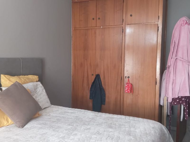 A bedroom featuring a large, floor-to-ceiling built-in wooden wardrobe with multiple storage compartments.