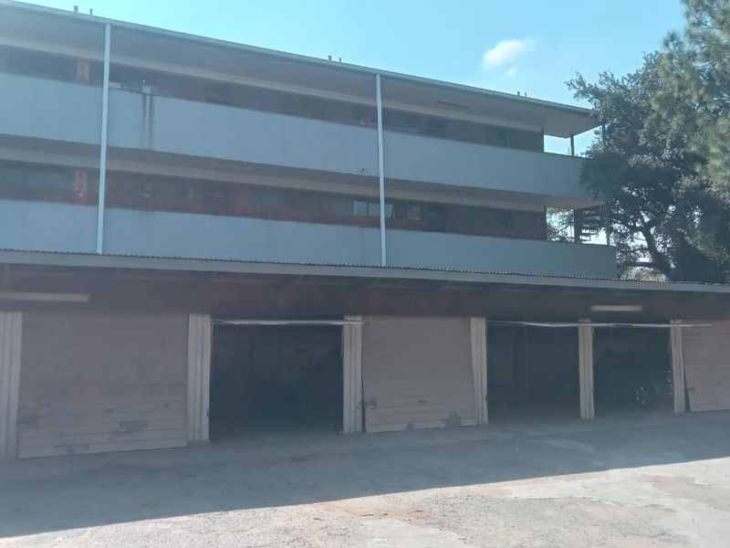 Exterior view of a multi-level apartment building featuring a row of covered parking bays with metal garage doors and a concrete driveway.