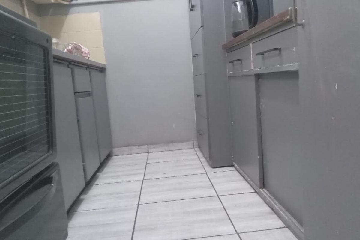 A compact kitchen featuring built-in cabinetry, tiled flooring, and a built-in oven, offering a functional layout in need of cosmetic updates.